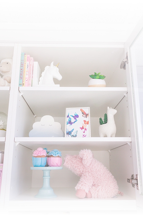 Bookcase shelves with toys (a unicorn, books, butterflies, llama, piggy, plant, cupcakes)at a Kids Reconnect playroom