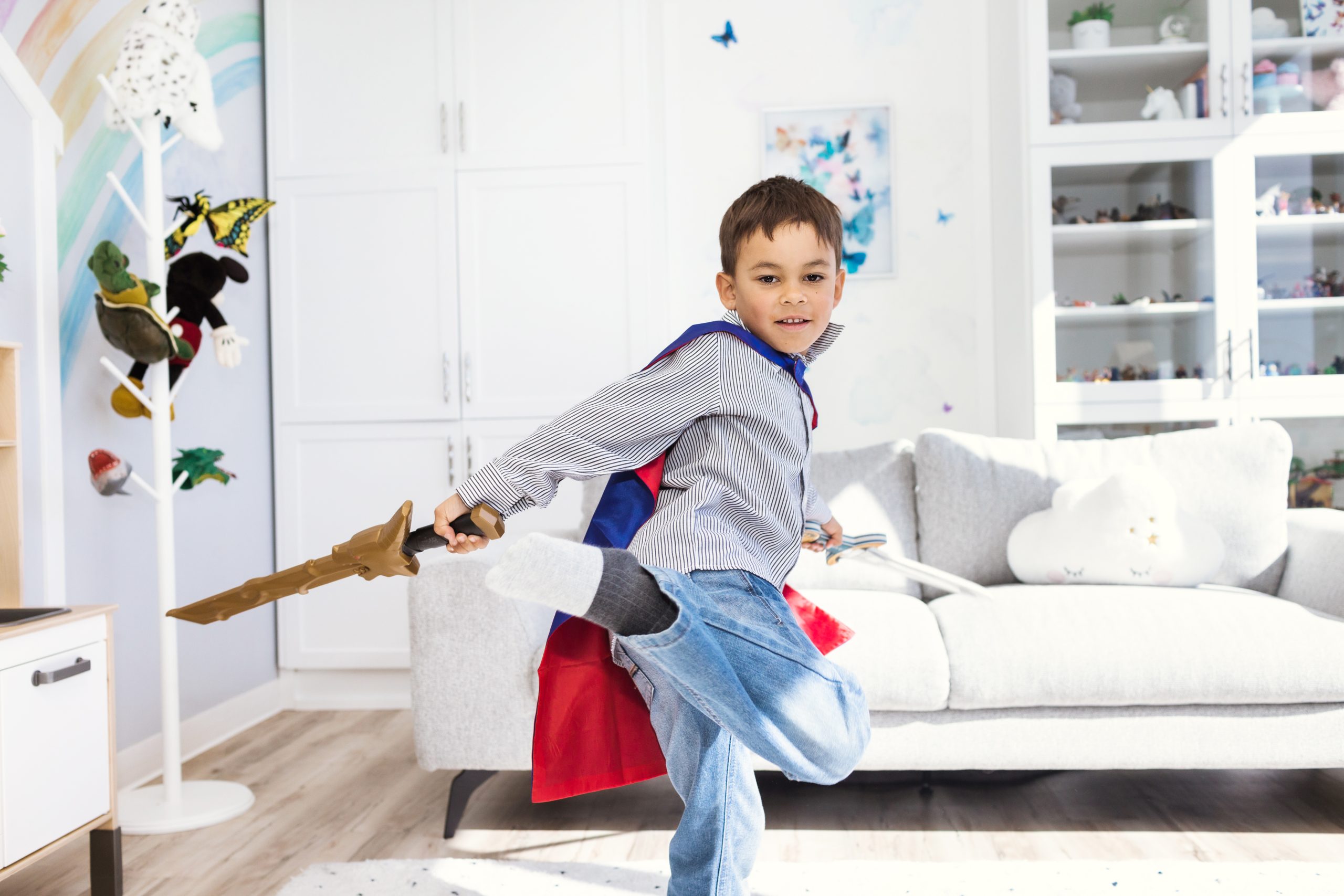 A child, wearing a red and blue cape, brandishes a plastic sword, while skillfully performing a turnkick