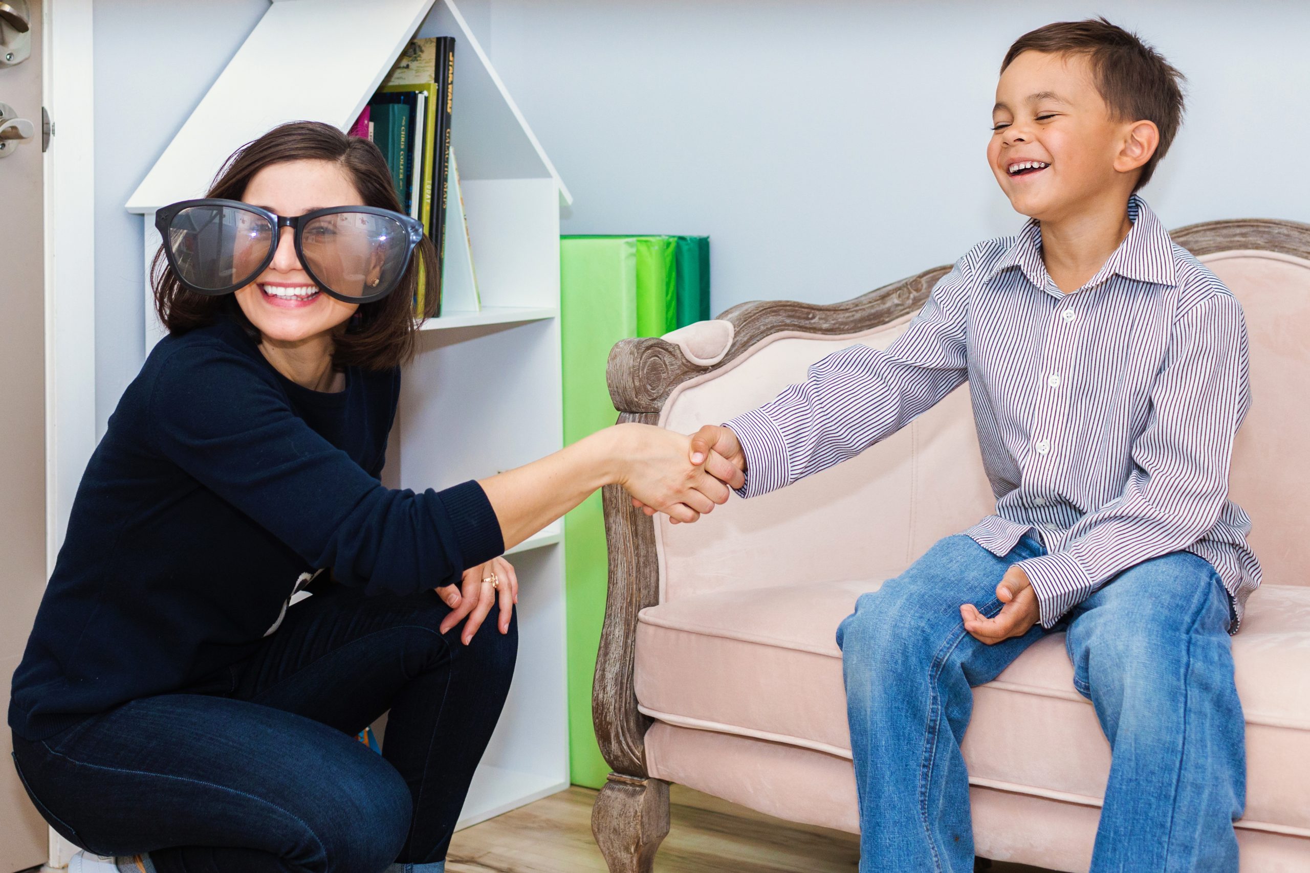 A laughing child shaking hands with his play therapist. The therapist is wearing giant sunglasses.