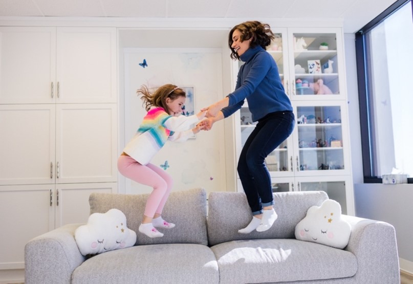 A child and her therapist joyfully jumping on a sofa during a play therapy session