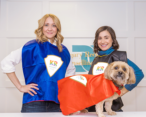 Therapists and dog, wearing capes with the Kids Reconnect logo