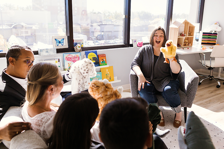 A father, mother, and two children interacting with a family therapist at Kids Reconnect. The therapist is using a fluffy yellow duck puppet