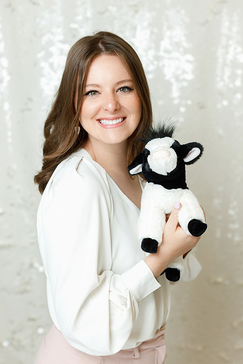 Headshot: Katie Musgrove, MEd, RPsych, child therapist at Kids Reconnect. Katie is smiling as she holds a fluffy cow stuffy. The cow is smiling too!