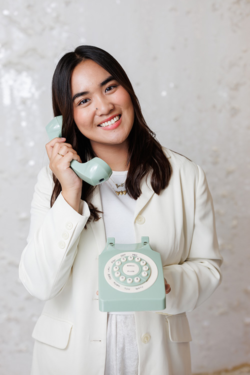 Mary Molina, Intake Specialist at Kids Reconnect, smiling as she poses with a toy retro rotary phone.