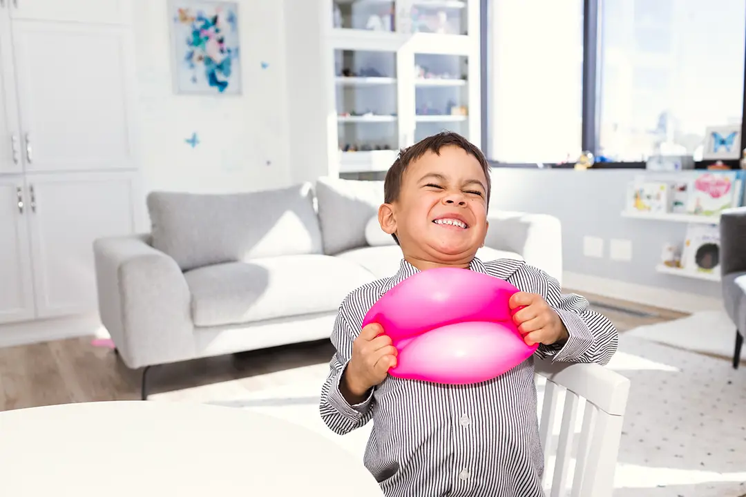 A child in a playroom. His eyes are closed, and he is tugging at a stretchy stress ball with all his might.