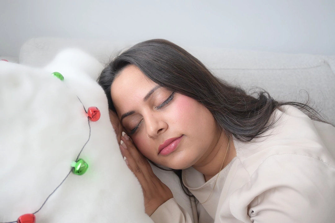 A woman sleeping on. a fluffy pillow. Holiday lights are strung over the pillow.