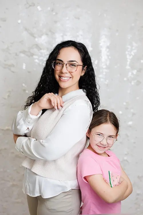 A child counsellor (Rita Motta) and a young girl smilie as they stand with their backs to each other. The girl is wearing a t-shirt with a watermelon sequin design.