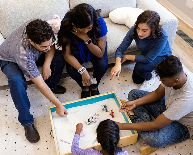 Overhead view of Dad, Mom, and two kids doing sand tray therapy with a child psychologist