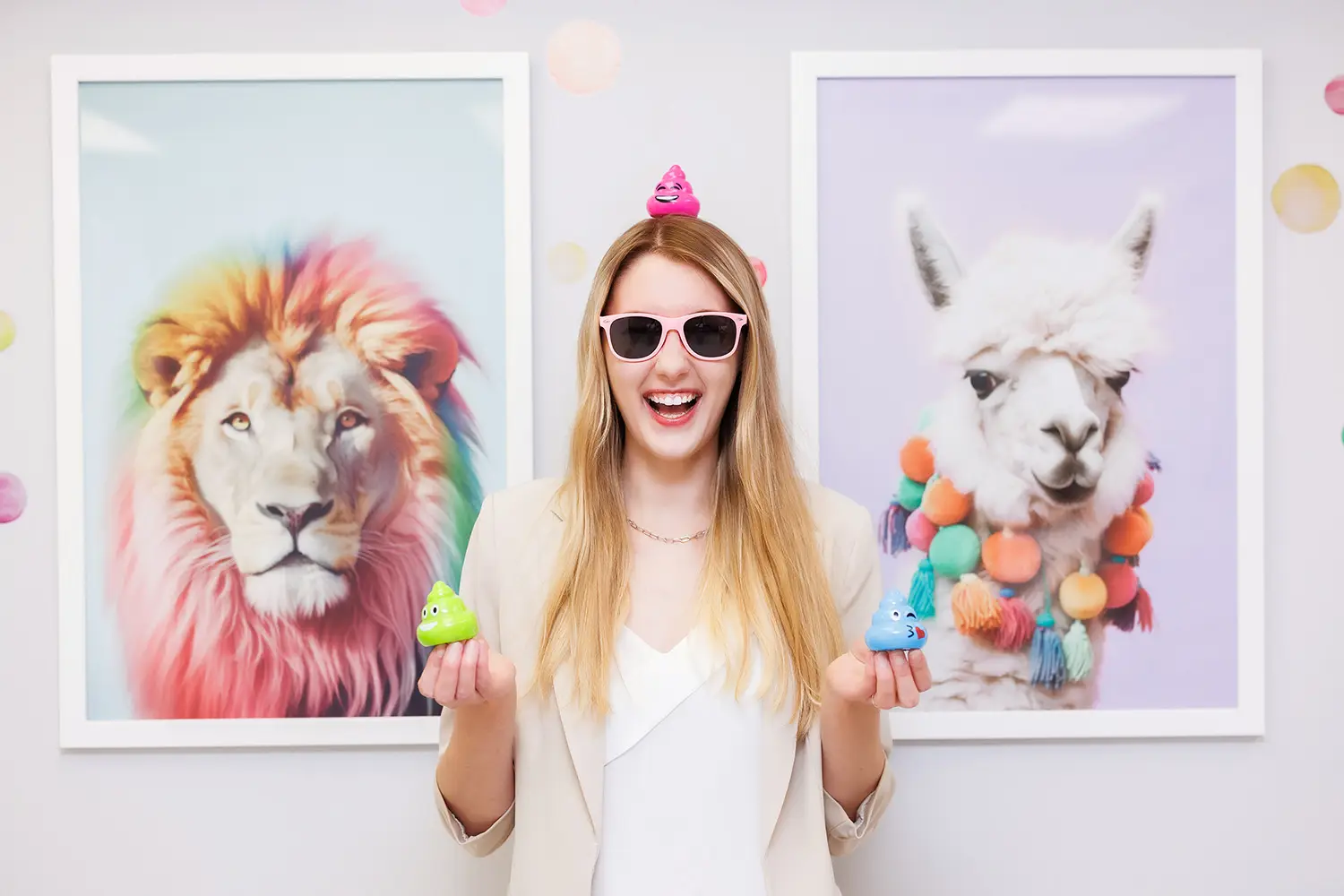 A child therapist wearing sunglasses smiles as she balances three "poop" emojis: one on her head, and one on each hand. In the background, a picture of a llama wearing a rainbow pompons necklace, and a lion with a rainbow coloured mane. This is Liza Eldysheva, a Practicum Student at Kids Reconnect, who co-facilitates the Feelings and Friends Group at Kids Reconnect.