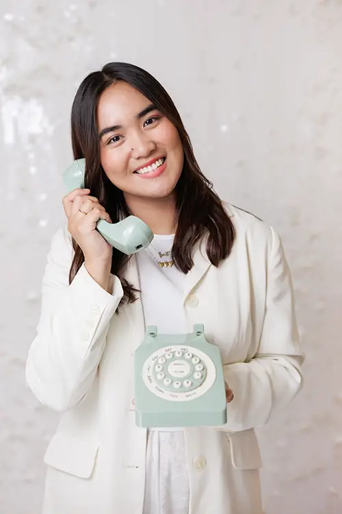 Mary Molina, Intake Specialist at Kids Reconnect, smiling as she playfully poses with a retro rotary phone.