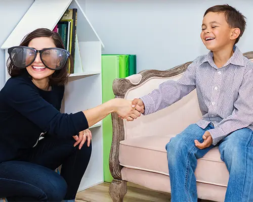 A laughing child shaking hands with his play therapist. The therapist is wearing giant sunglasses.