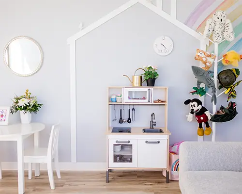 Playfully equipped playroom at Kids Reconnect. A rainbow mural, plush toys hanging on a perch, and a toy kitchen await.