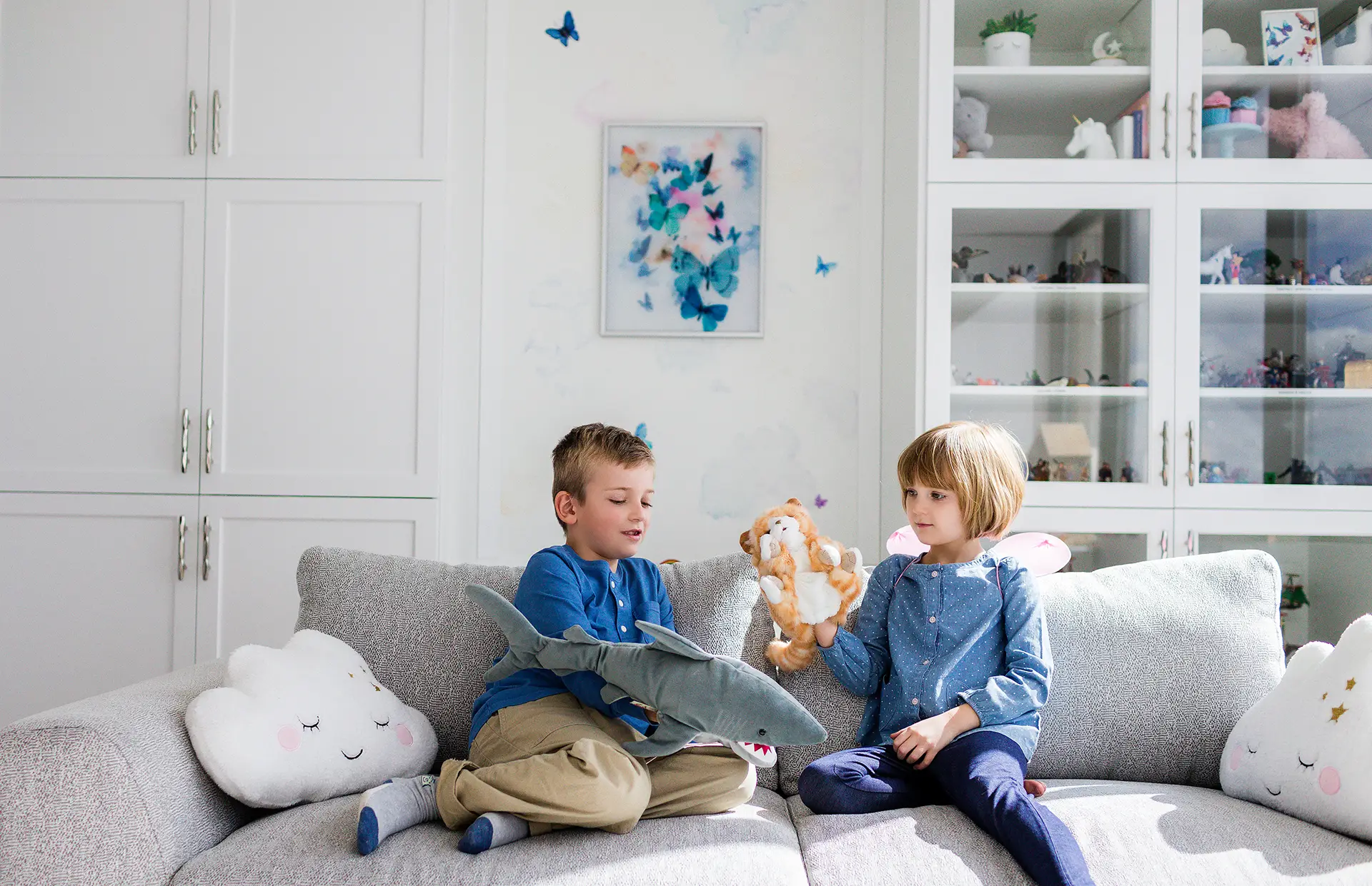 Two siblings sitting on a couch in a play therapy session at Kids Reconnect. The boy is playing with a shark puppet, and the girl is playing with a cat puppet.