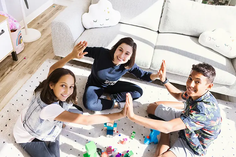 Two kids and a child therapist sitting cross-legged in a playroom, high-give each other during a specialized child counselling session