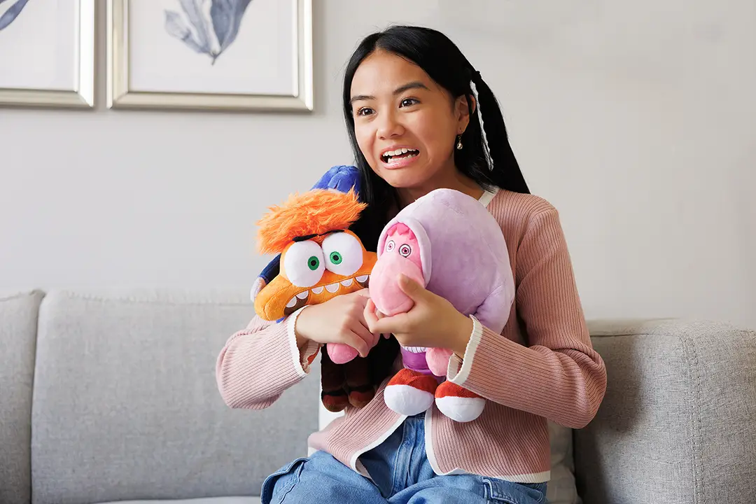 A girl with an anxious expression grits her teeth as she holds two stuffies. She is sitting on a therapy couch.