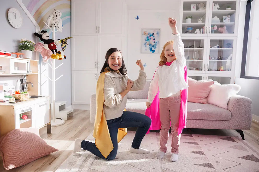 Child psychologist Marcella Galizia with a girl in a playroom, showing their power poses and wearing Superhero capes.