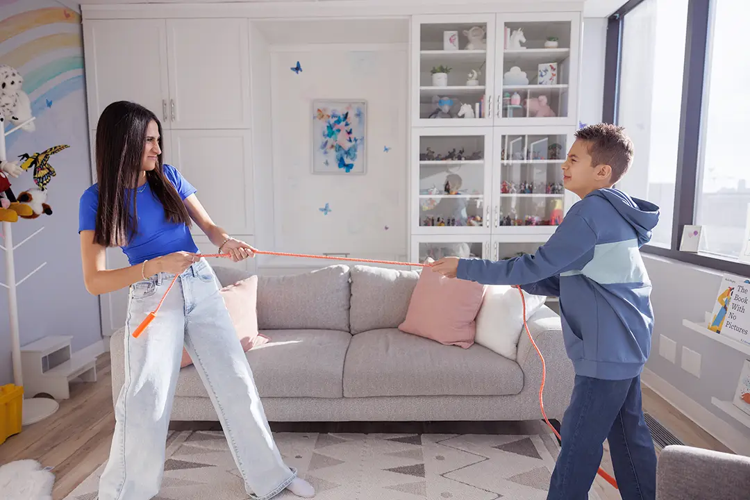 Playing with kids of different ages A teenage girl and a school-age boy playfully grimacing as they play ”tug-of-war” with a rope in a playroom